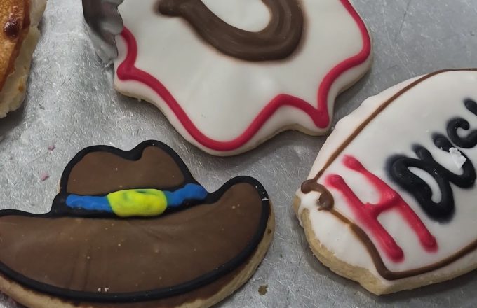 Texas-themed decorated sugar cookies shaped like a horseshoe, cowboy hat, and Houston text on a metal tray with tongs at Arandas Bakery