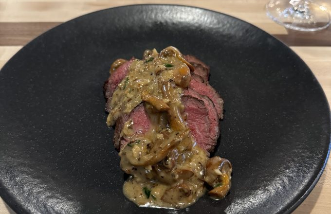 Sliced rare beef with mushroom sauce on a black plate at Barbacana