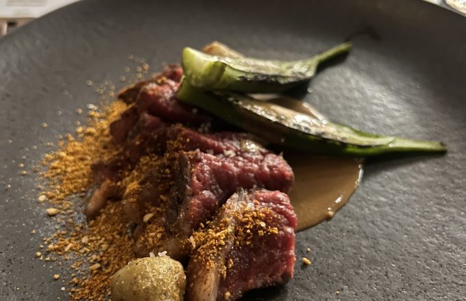 Sliced rare steak with charred peppers, spice dust, and sauce on a black plate at Barbacana