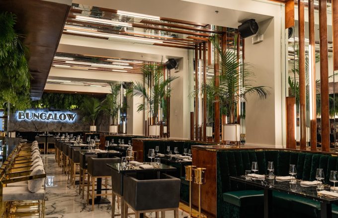 Upscale dining room with green velvet booths, gold bar stools, marble floors, and palm plants at Barbacana