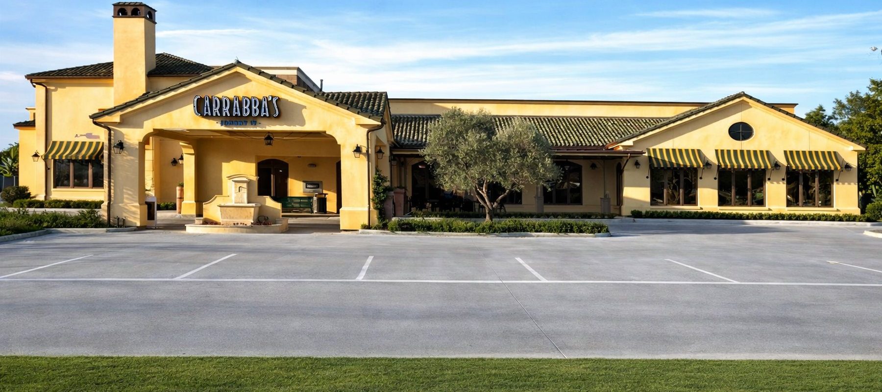 Exterior of Carrabba's on Kirby with Tuscan-style yellow stucco facade clay tile roof striped awnings and fountain entrance in Houston