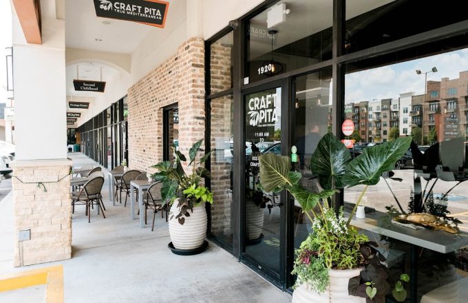 Brick storefront with Craft Pita signage, large potted tropical plants, and outdoor patio seating at Craft Pita