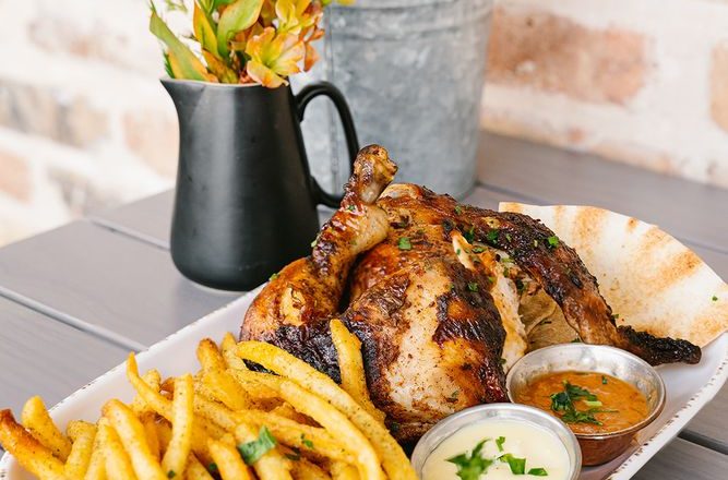 Half bird roasted chicken with crispy golden fries on a plate at Craft Pita — Fountain View