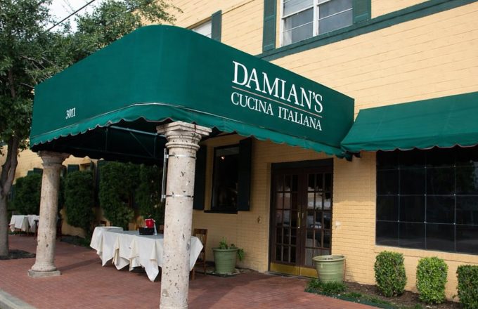 Historical exterior of Damian's Cucina Italiana with green awning yellow building stone columns and outdoor seating on Smith Street in Houston