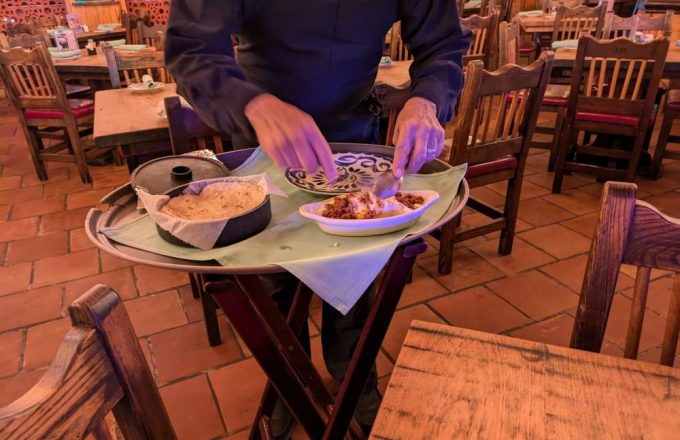 Server presenting a tray of choriqueso dip with white queso chips and salsa in the dining room at El Tiempo Cantina — Navigation