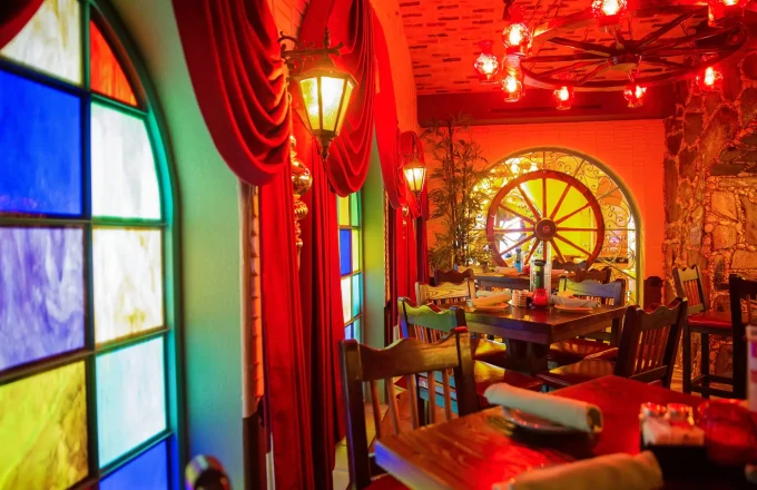 Interior dining room with stained glass windows rustic wooden chairs and warm red ambient lighting at El Tiempo Cantina — Navigation