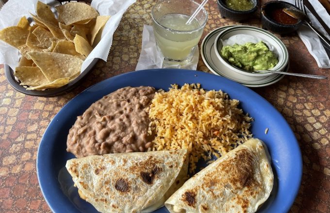 Quesadillas with rice and refried beans on a blue plate with chips, guacamole, and a margarita at La Mexicana
