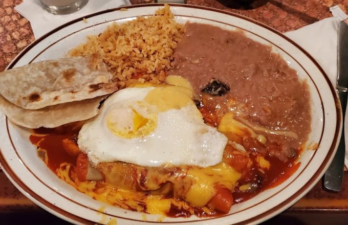 Chilaquiles topped with a fried egg, served with rice, refried beans, and a flour tortilla on a brown-rimmed plate at La Mexicana