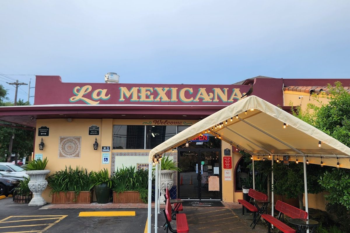 Yellow building with La Mexicana sign, covered canopy tent with string lights, and red patio benches at La Mexicana