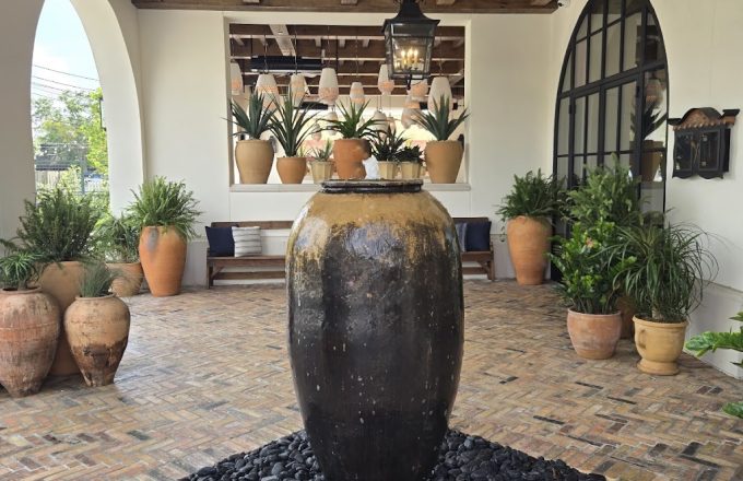 Entrance courtyard of Latuli restaurant with large dark fountain vase brick herringbone flooring arched windows and southwestern-inspired decor in Houston