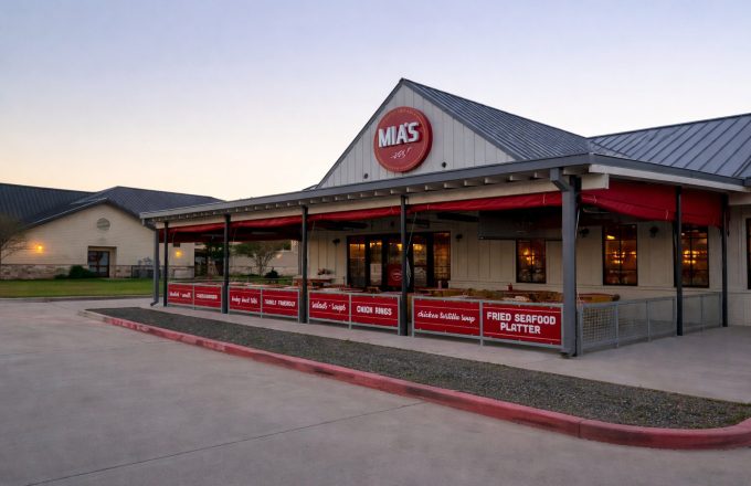 Exterior of Mia's Table Cypress location with red awnings, covered patio seating, and round Mia's Table sign