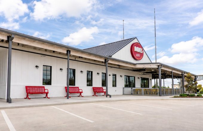 Exterior of Mia's Table Katy location with red benches, round Mia's Table sign, and covered patio entrance