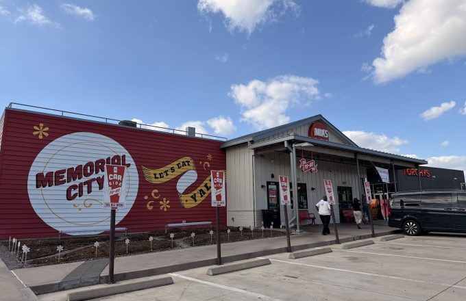 Exterior of Mia's Table Memorial City location with red Memorial City mural, Let's Eat Y'all banner, and round Mia's Table sign