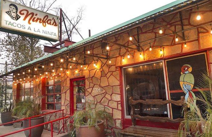 Stone building exterior with iconic Ninfa's Tacos a la Ninfa sign, string lights, and painted parrot mural at Ninfa's on Navigation
