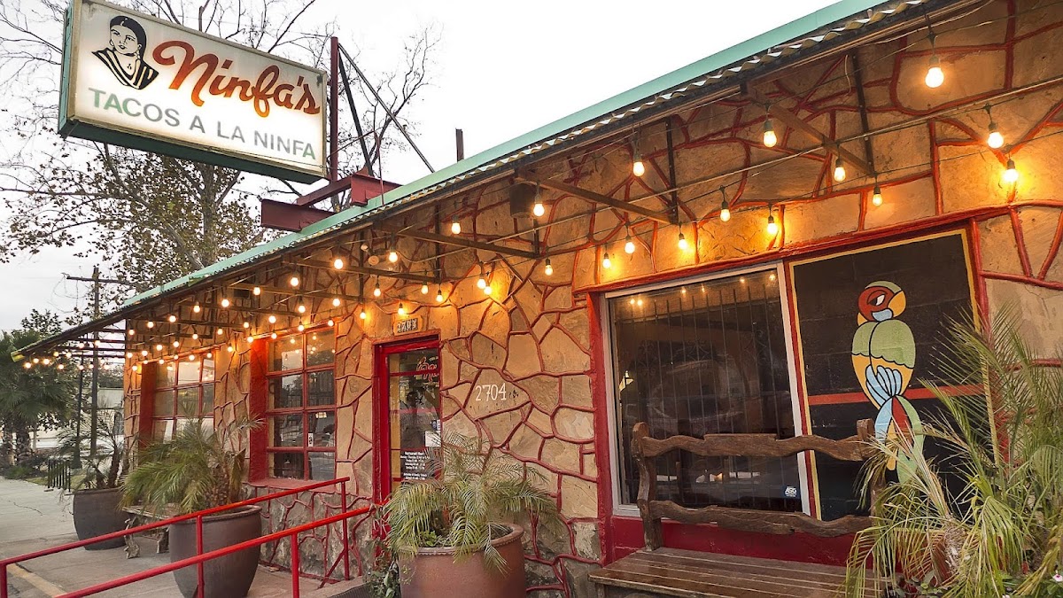 Stone building exterior with iconic Ninfa's Tacos a la Ninfa sign, string lights, and painted parrot mural at Ninfa's on Navigation