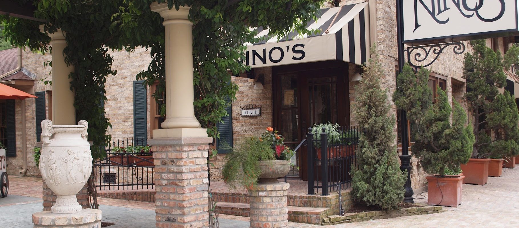 Historical exterior of Nino's Italian restaurant with Nino's sign brick facade striped awning columns and Tuscan courtyard on West Dallas Street in Houston