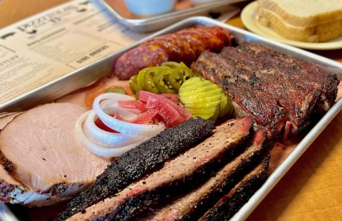 BBQ tray with sliced brisket ribs sausage pickles onions and sides at Pizzitola's Heritage BBQ