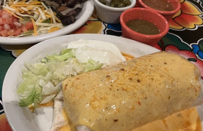 Smothered burrito with queso sauce, lettuce, and sour cream on a colorful floral tablecloth at Rio Grande Tex-Mex Grill