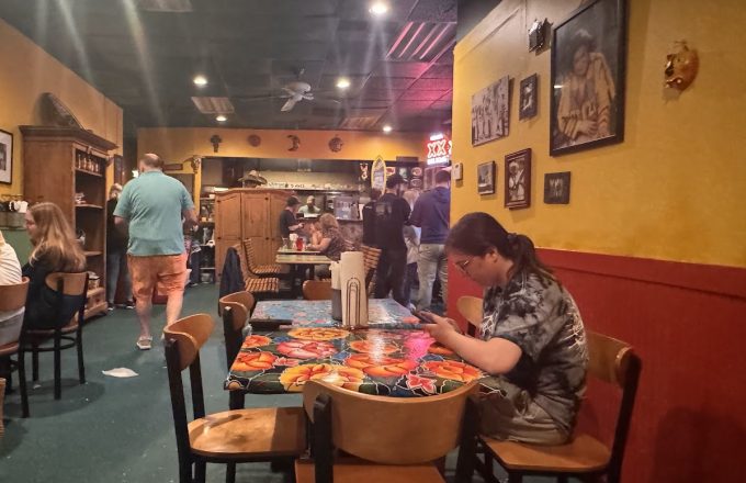 Dining room with colorful floral tablecloths, yellow and red walls, framed artwork, and wooden furniture at Rio Grande Tex-Mex Grill