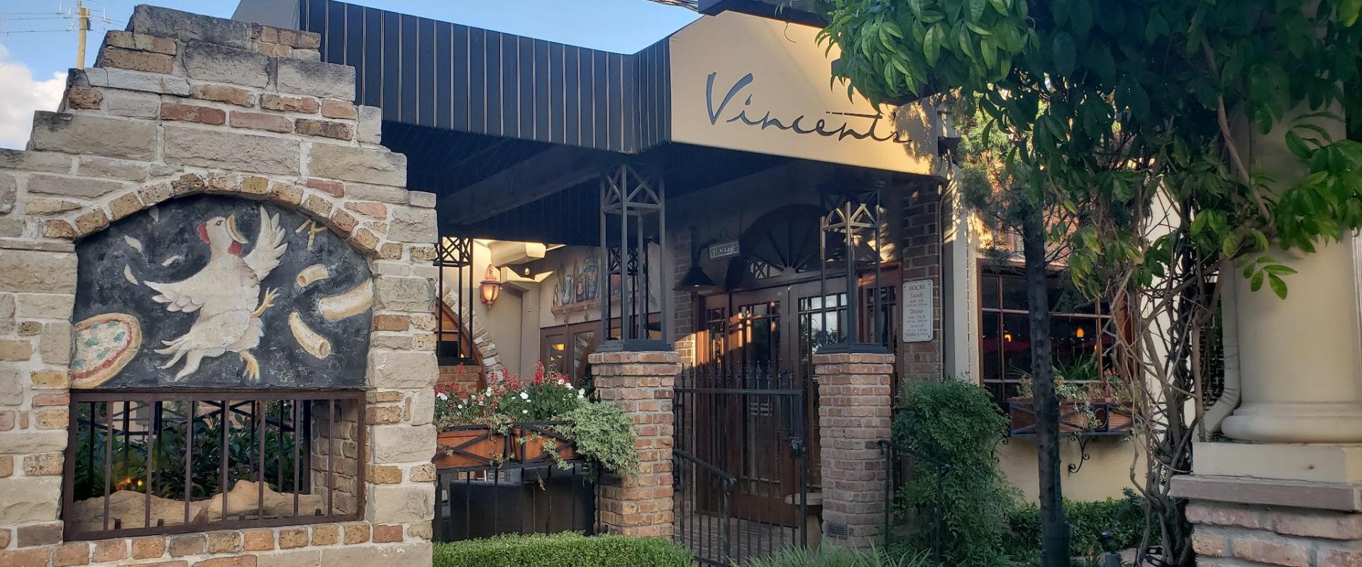 Historical exterior of Vincent's Italian restaurant with Vincent's sign stone facade rooster mural and Tuscan courtyard on West Dallas Street in Houston