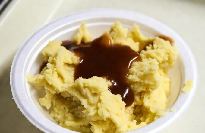 A generous mound of mashed potatoes crowned with brown gravy — comfort food dispensed with institutional precision and maternal intent.
