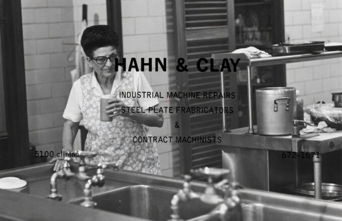 Mrs. Greer stands at the stainless pass in her floral apron, coffee cup in hand, surveying her kitchen. The black-and-white candid was later overlaid with text for a Hahn & Clay sponsor ad in the yearbook — but with the text removed it's the truest portrait of her we have: quietly in command of the room that fed a generation.
