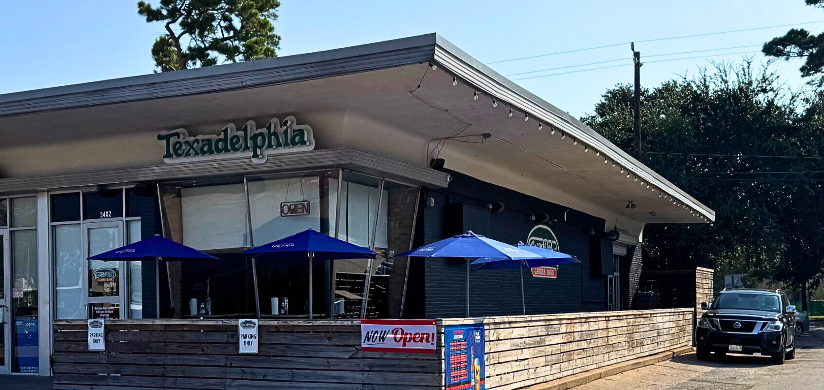 Texadelphia Garden Oaks cheesesteak restaurant exterior with blue patio umbrellas and signage