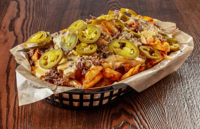 Texadelphia cheesesteak loaded waffle fries topped with melted queso, shaved steak, and jalapenos