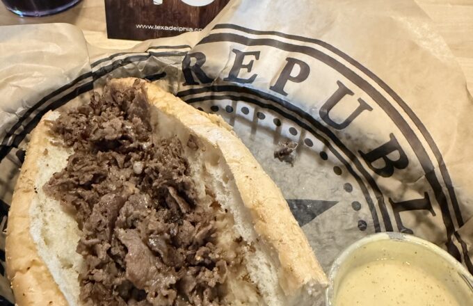 Classic Texadelphia cheesesteak sandwich on a hoagie roll with a side cup of queso, served on a 40th-anniversary Texadelphia tray