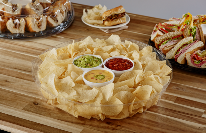 Texadelphia catering spread — tortilla chip platter with guacamole, salsa, and queso in the center, flanked by sandwich and wrap trays